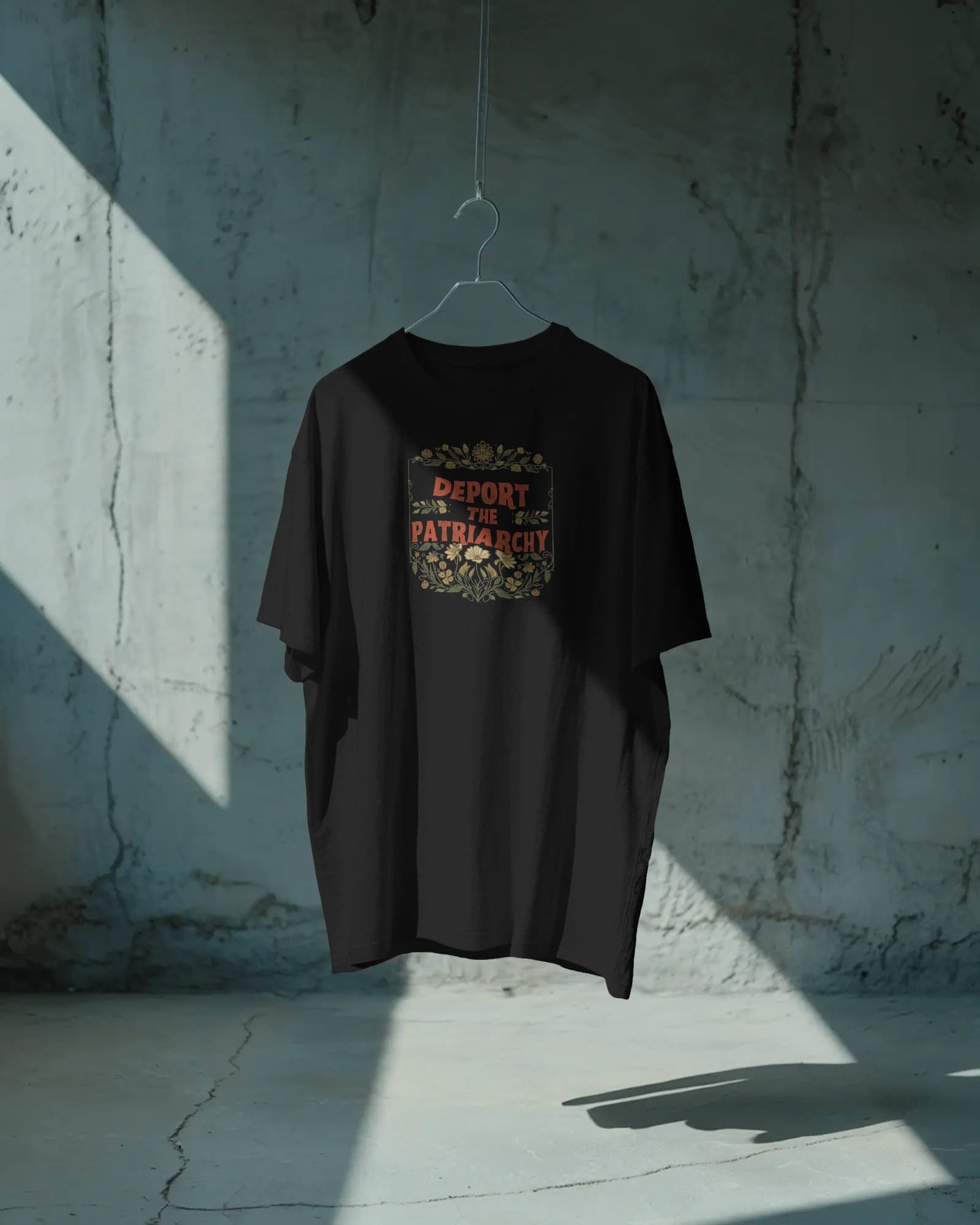 Deport the Patriarchy tee hanging against a raw concrete wall in dramatic natural light — Salt + Violet