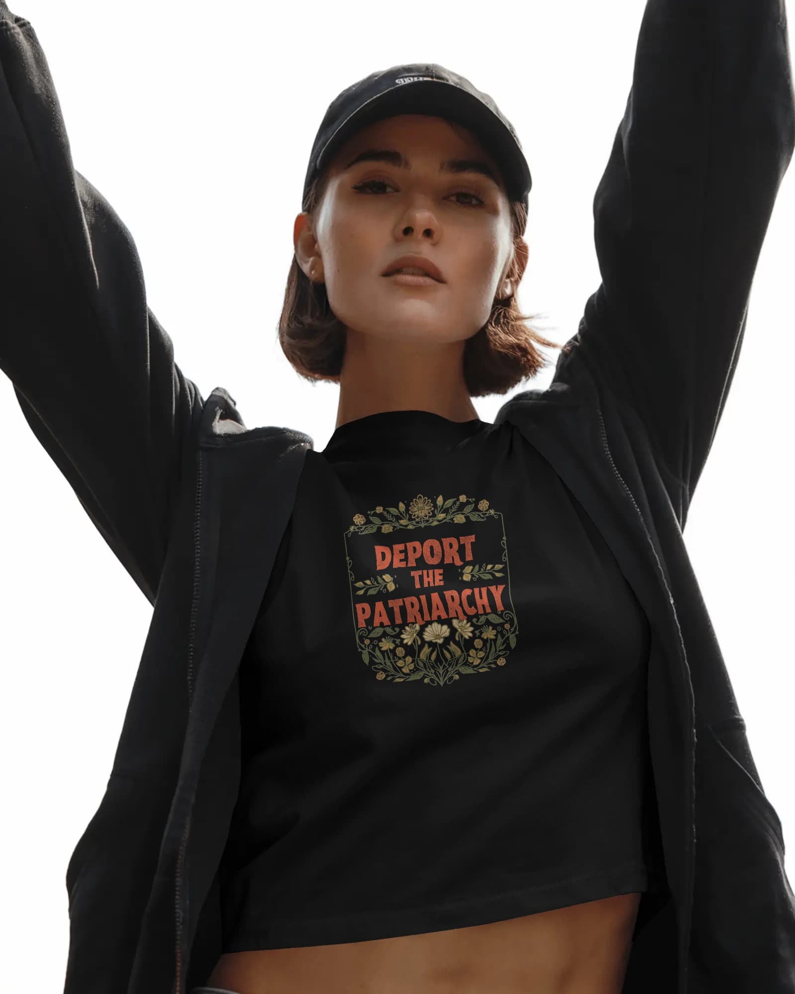 Deport the Patriarchy Tee — woman in black tee with botanical letterpress design, arms raised, confident pose
